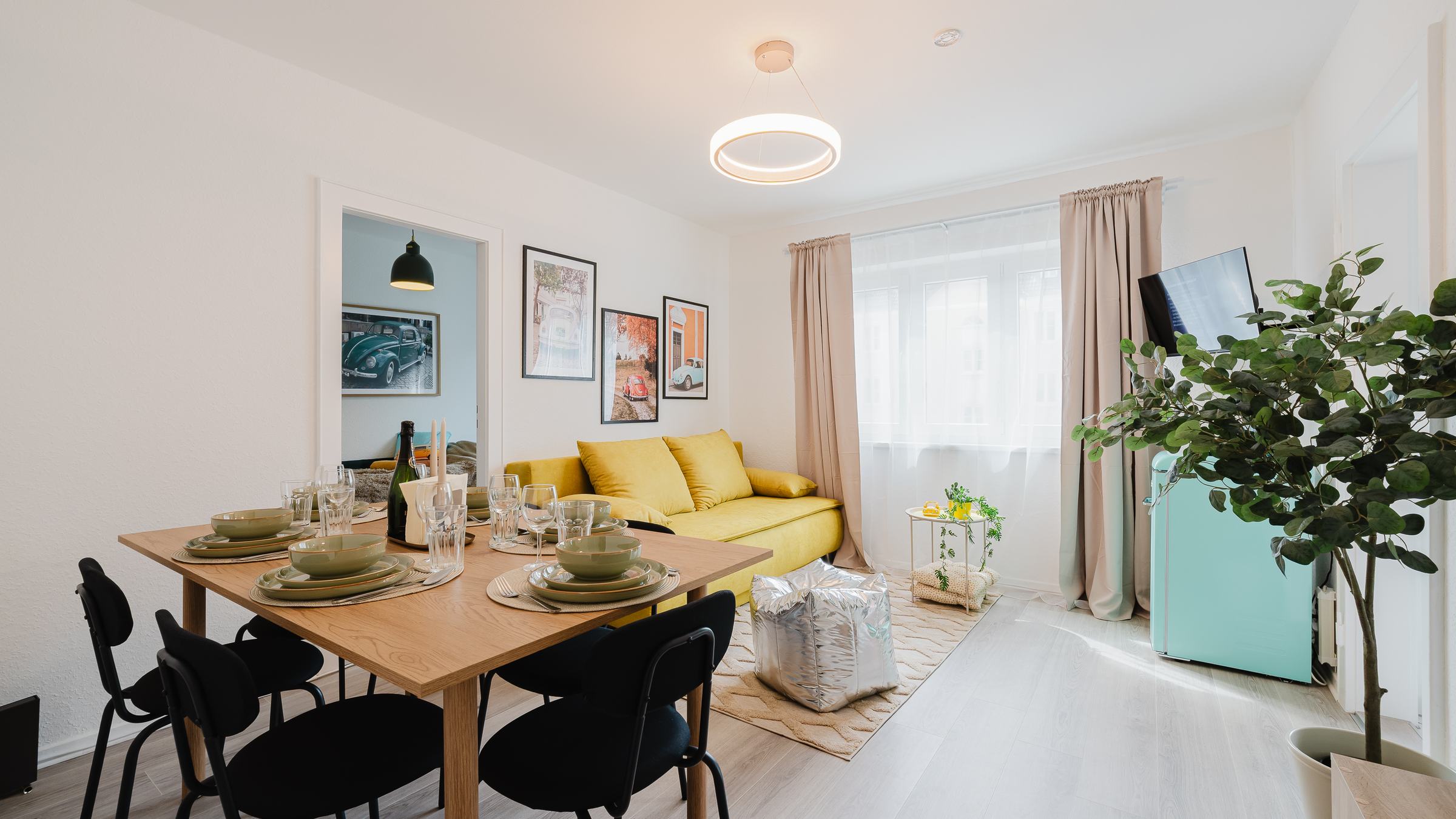 Heller Ess- und Wohnbereich im Beetle Apartment mit gedecktem Tisch, gelbem Sofa und Bilderwand