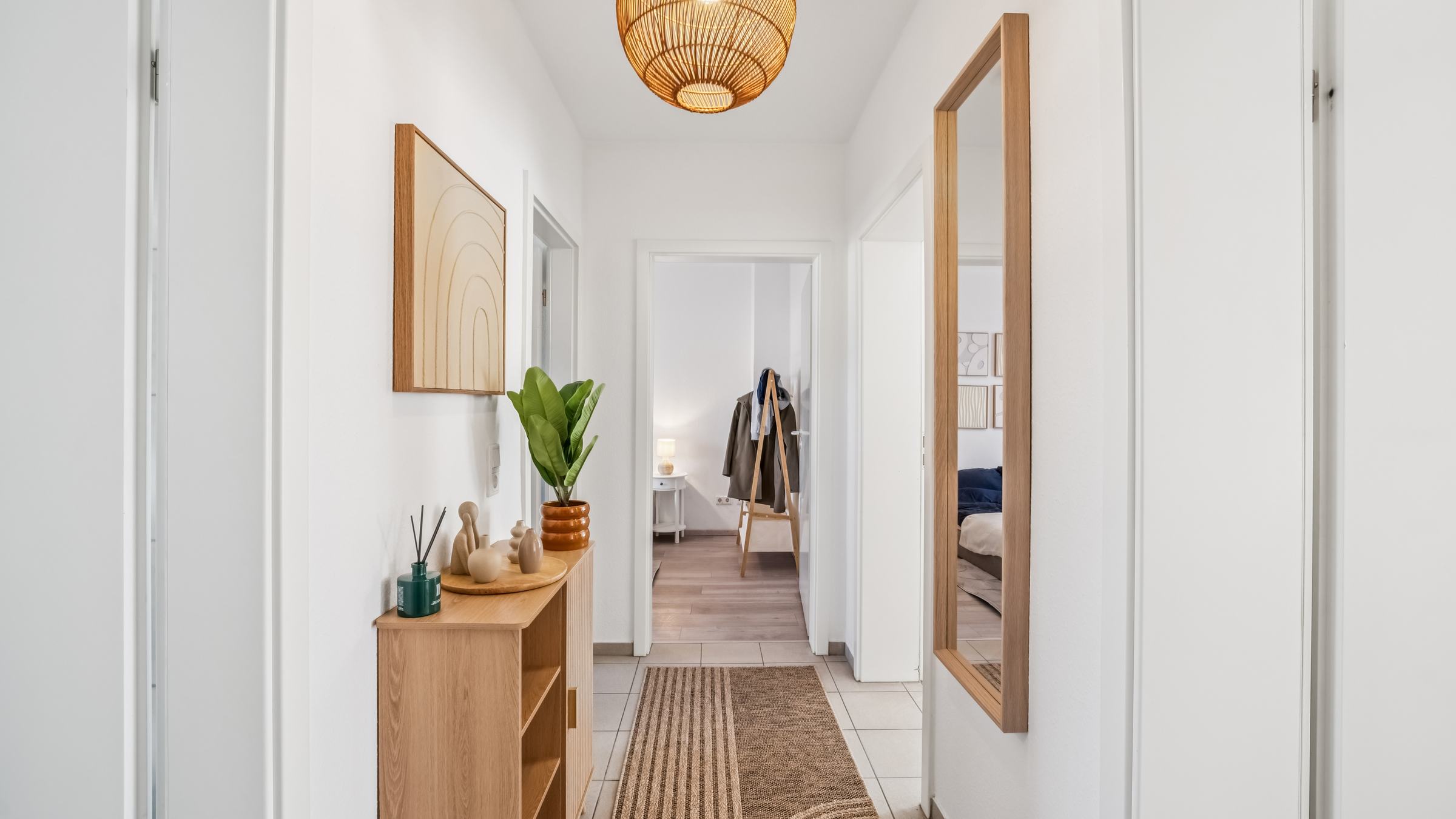 Flur mit Rattan-Pendelleuchte, Sideboard, Standspiegel und Blick ins Schlafzimmer